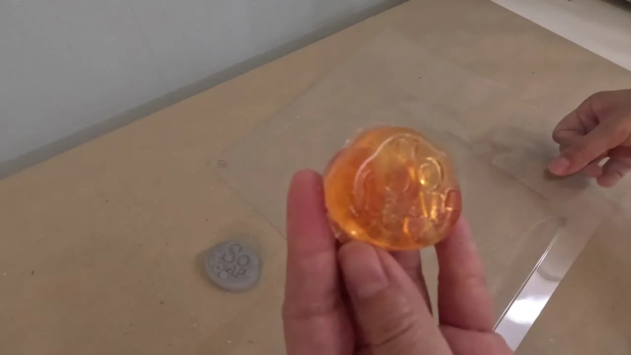 真空成形でできた型から取り出したオレンジ色の石鹸を手に持ち、奥にForm 4で造形したグレーの原型がある様子