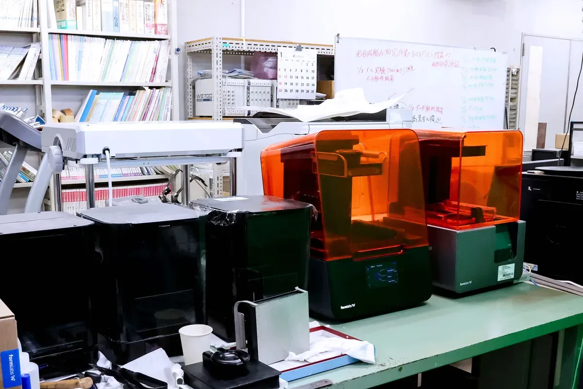研究室の棚に並ぶ光造形 3D プリンター 2 台と洗浄機