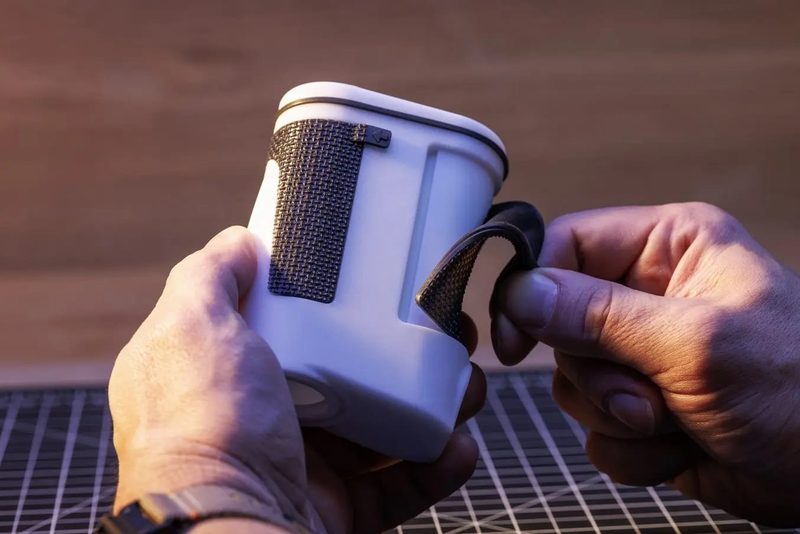 白い携帯機器の側面に、フレキシブル80A で造形した黒いグリップパッドを取り付けているところ