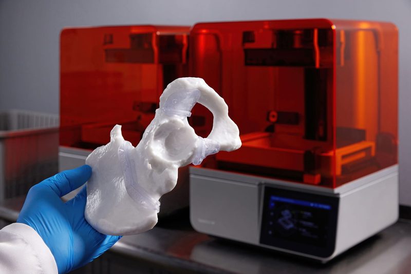 手袋をした手が持つ、ホワイトV5 で造形した骨格モデルと 3D プリンター