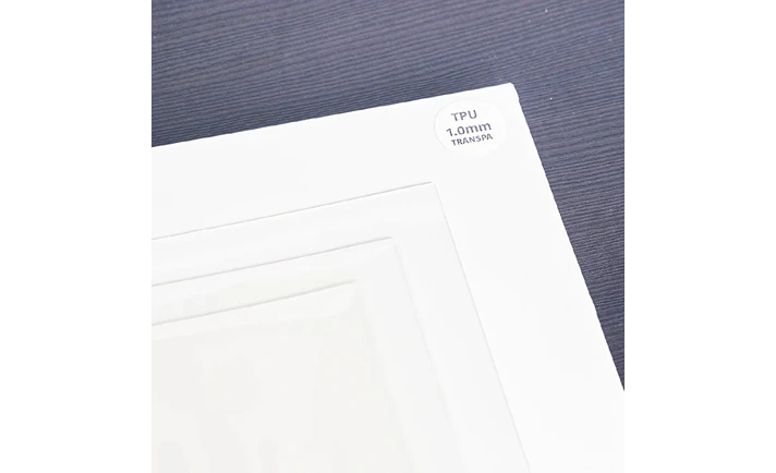 重ねた透明な TPU シートの角の接写。角に TPU と書かれた丸いラベルが貼られている